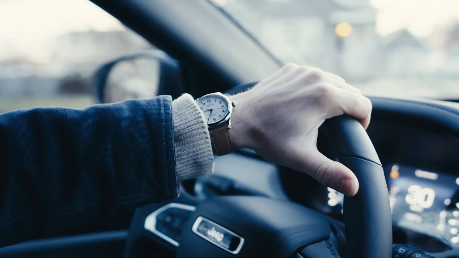 A hand resting on a steering wheel, wristwatch visible