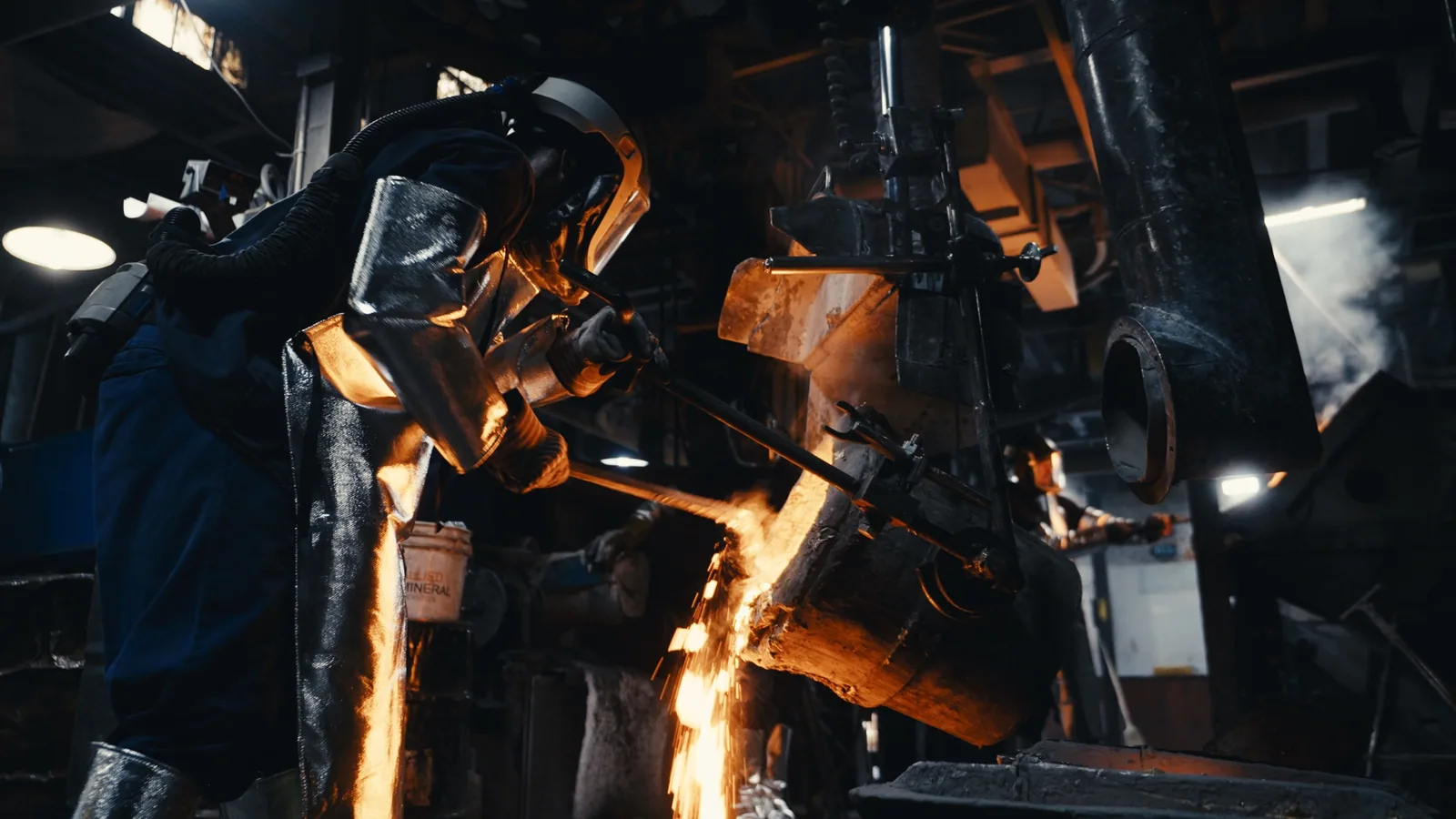 Molten metal glowing orange as it pours from a ladle in a foundry