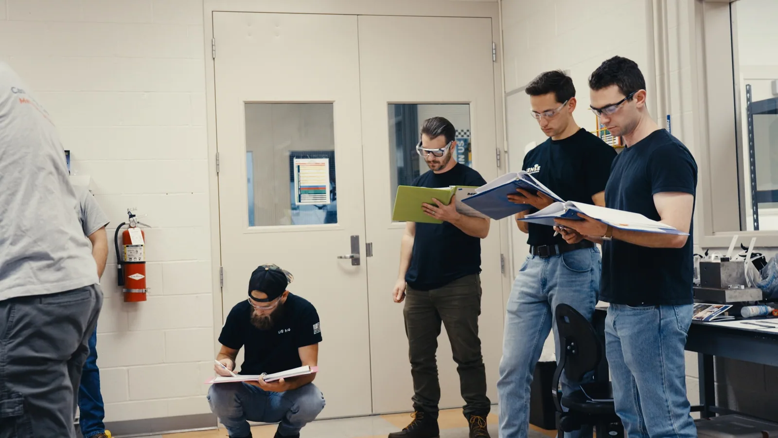 Bootcamp attendees reading manuals in a workshop classroom, one crouched taking notes