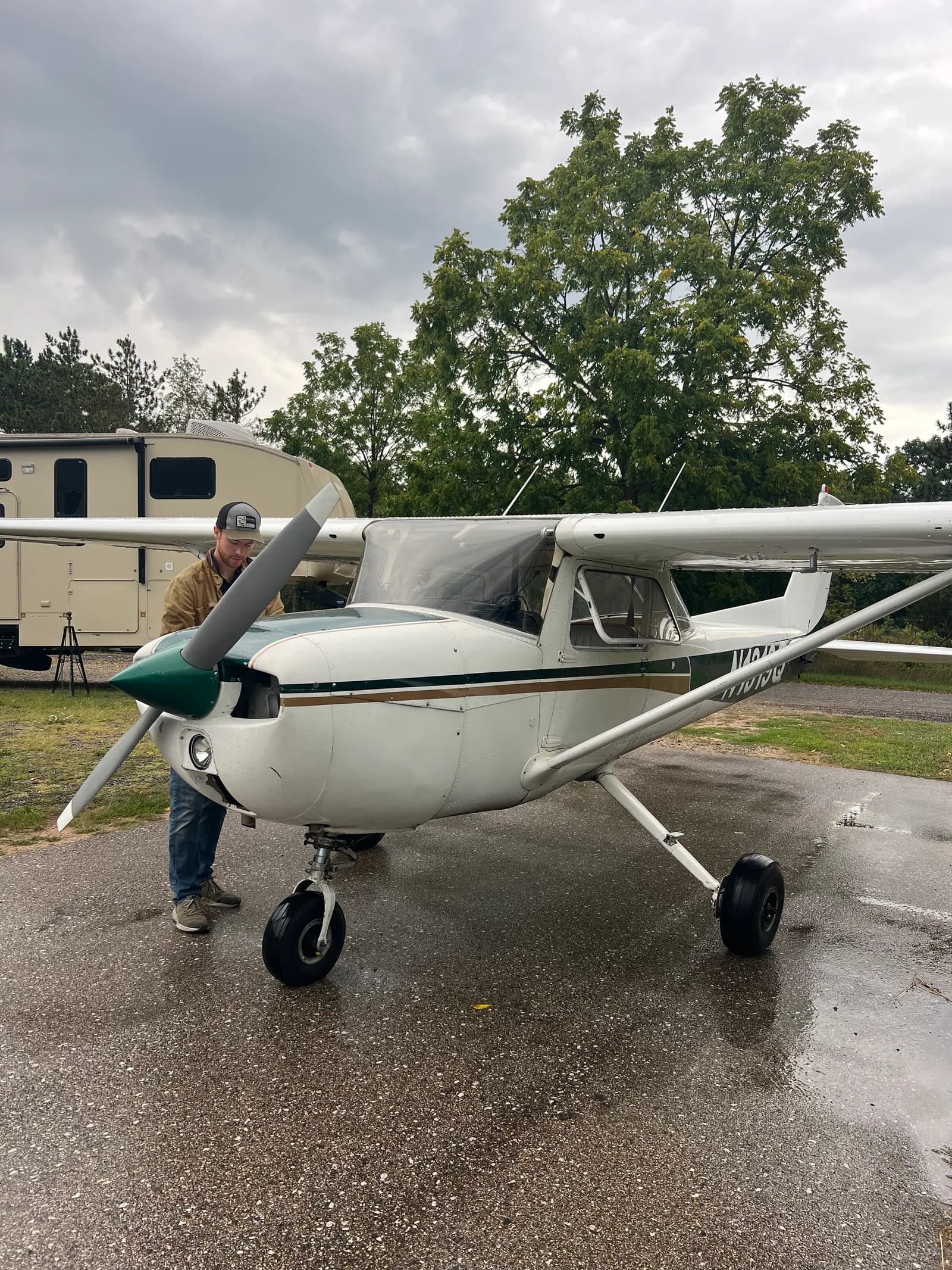 A single-engine Cessna parked on wet tarmac, a man walking past its wing