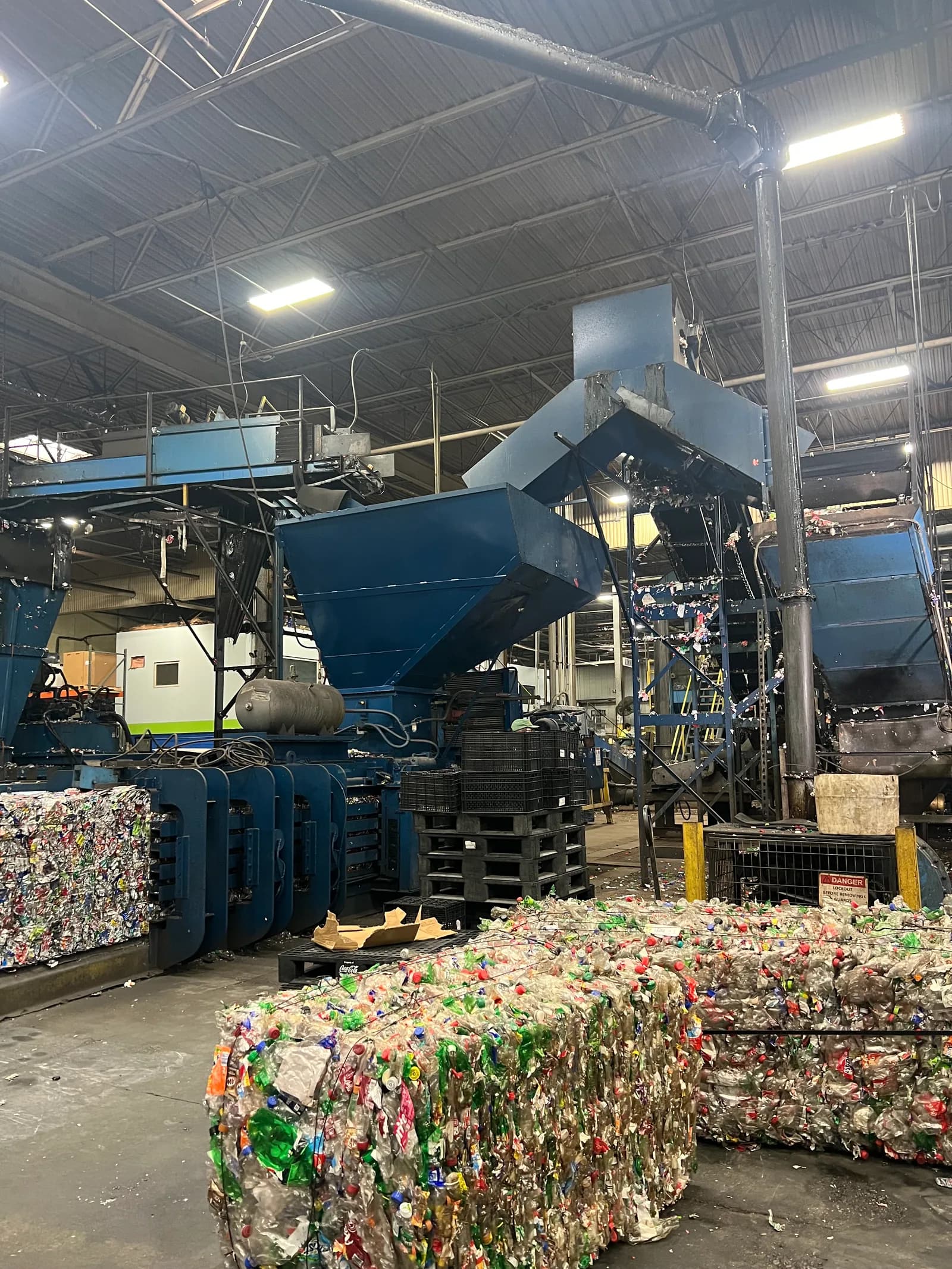 Blue sorting machinery inside a recycling plant, beside a mound of loose recyclables