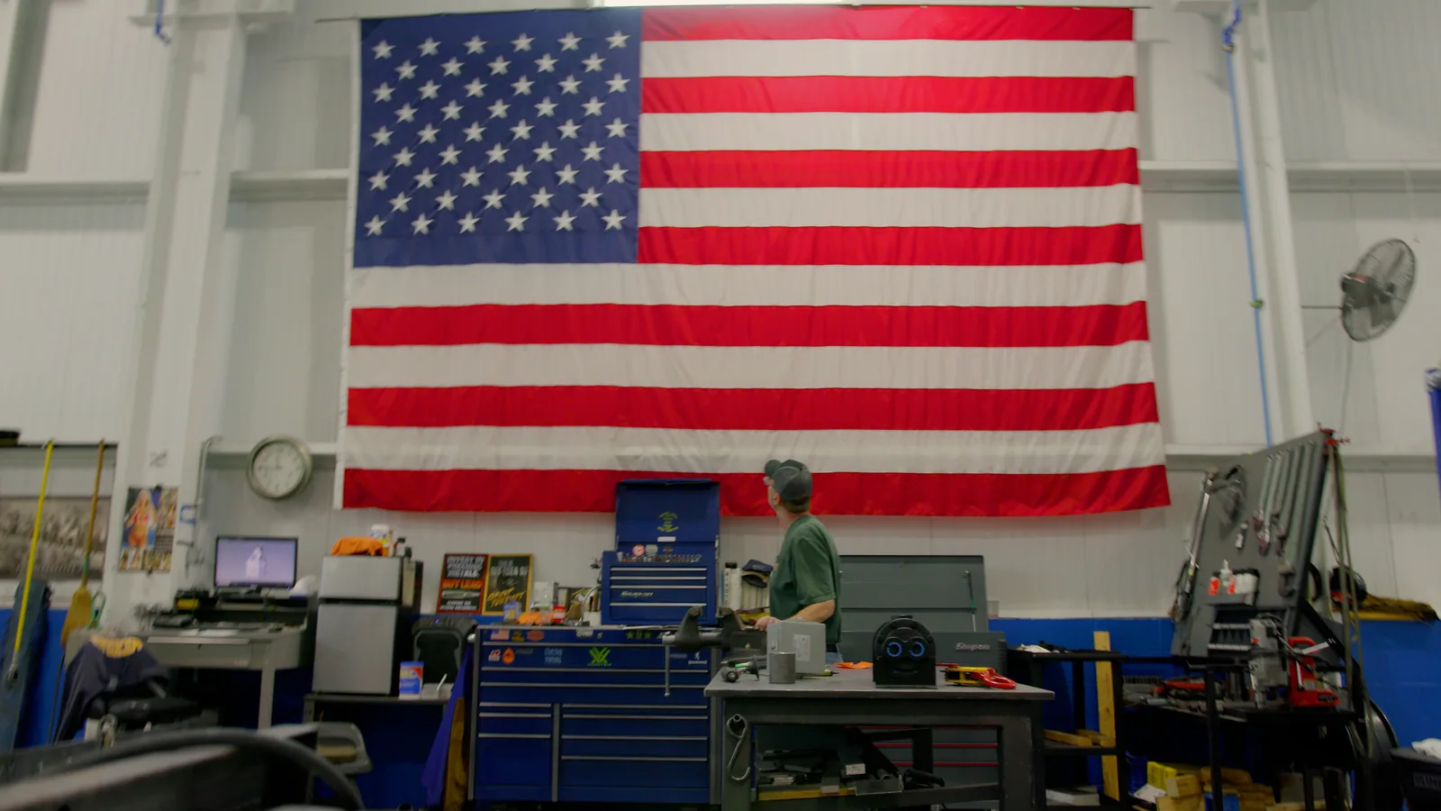 A large American flag hung above a workbench and red tool chests in a shop