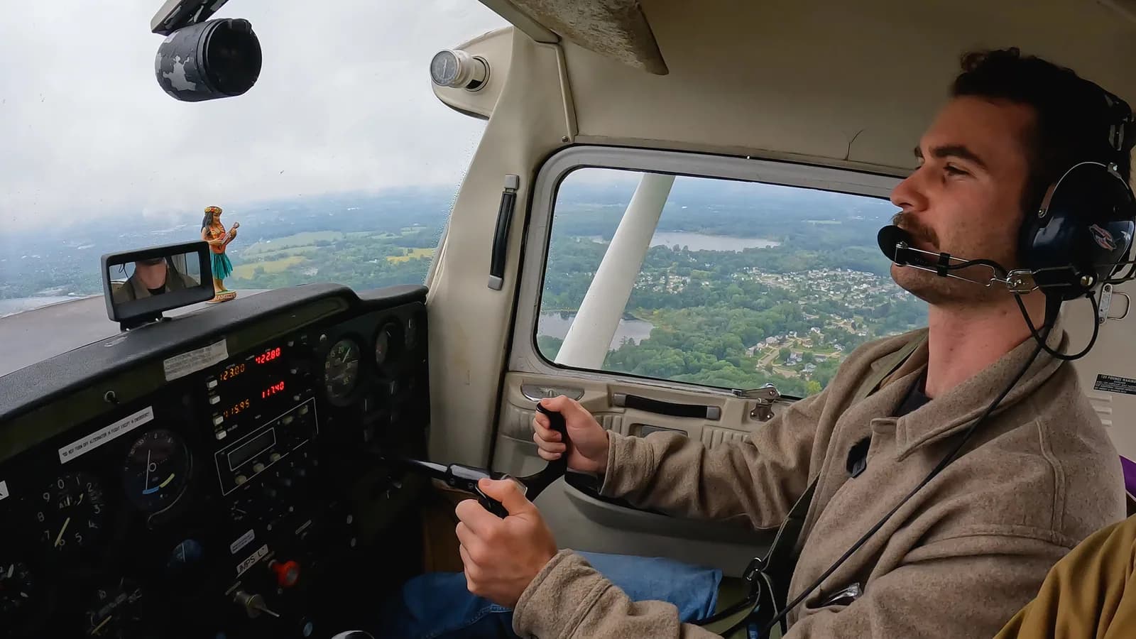Hands on the controls in a small aircraft cockpit, farmland through the window