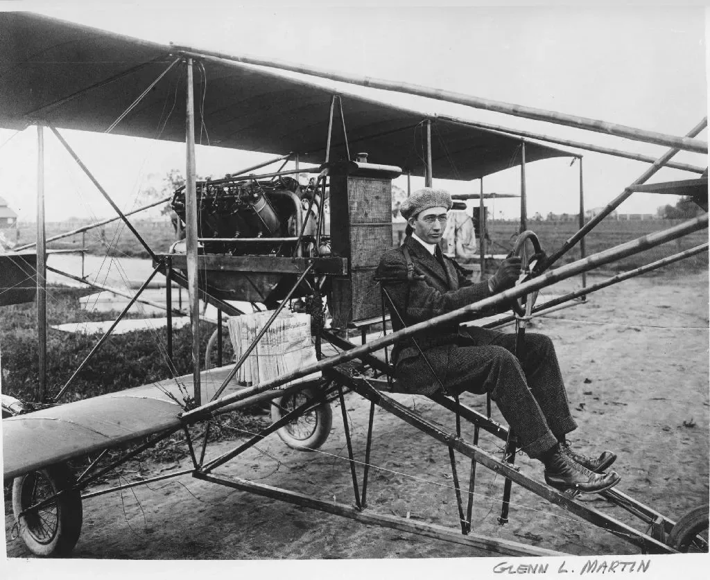 Glenn L. Martin seated at the controls of an early open-frame biplane on a grass field